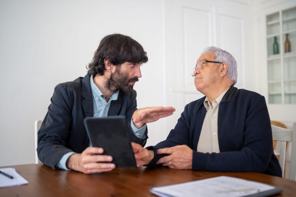 Two men having a professional discussion with a digital tablet at a wooden table indoors.
