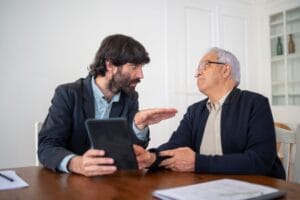 Two men having a professional discussion with a digital tablet at a wooden table indoors.