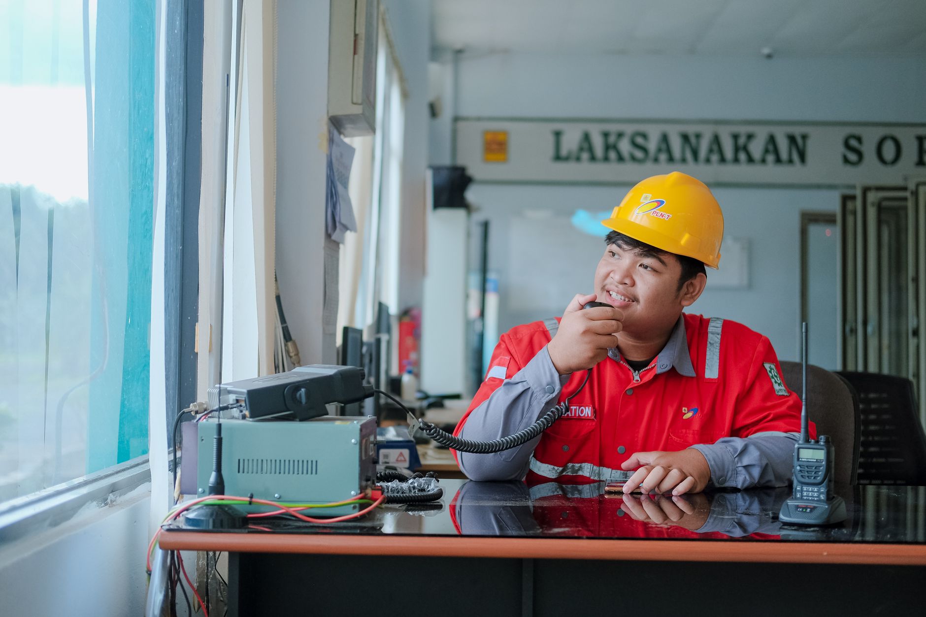 Smiling construction worker in hard hat using a two-way radio indoors for communication.