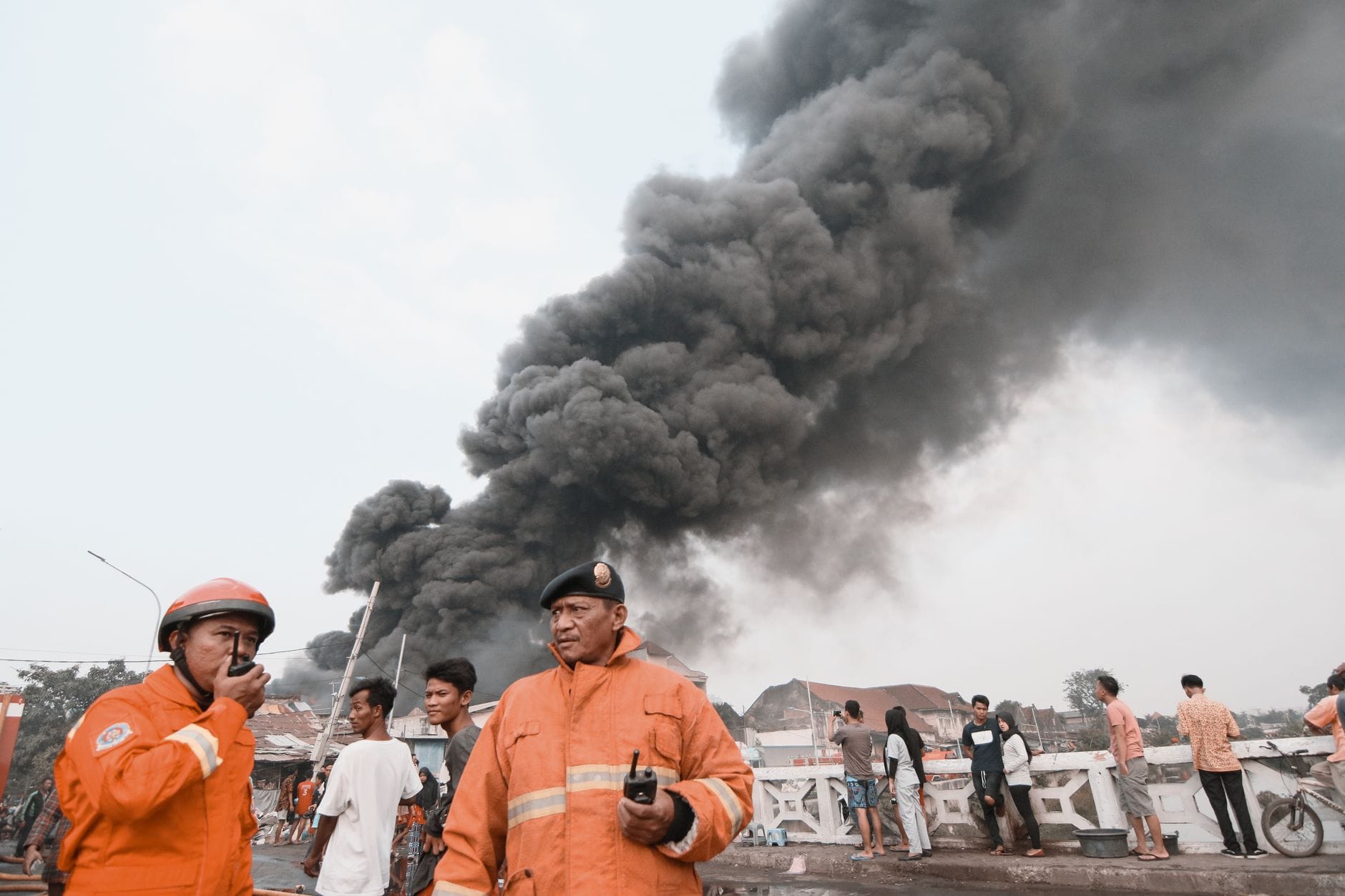 Firefighters in protective suits managing a chaotic situation with heavy smoke in the background. Emergency response underway.