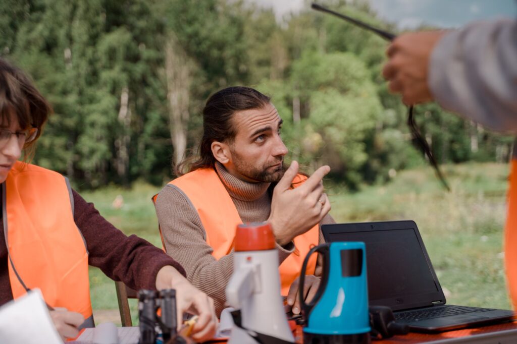 Volunteers in orange vests coordinating efforts outdoors with laptops and walkie talkies.