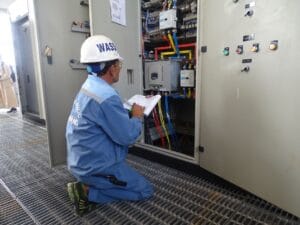 Engineer in uniform inspecting an electrical control panel in an industrial setting.