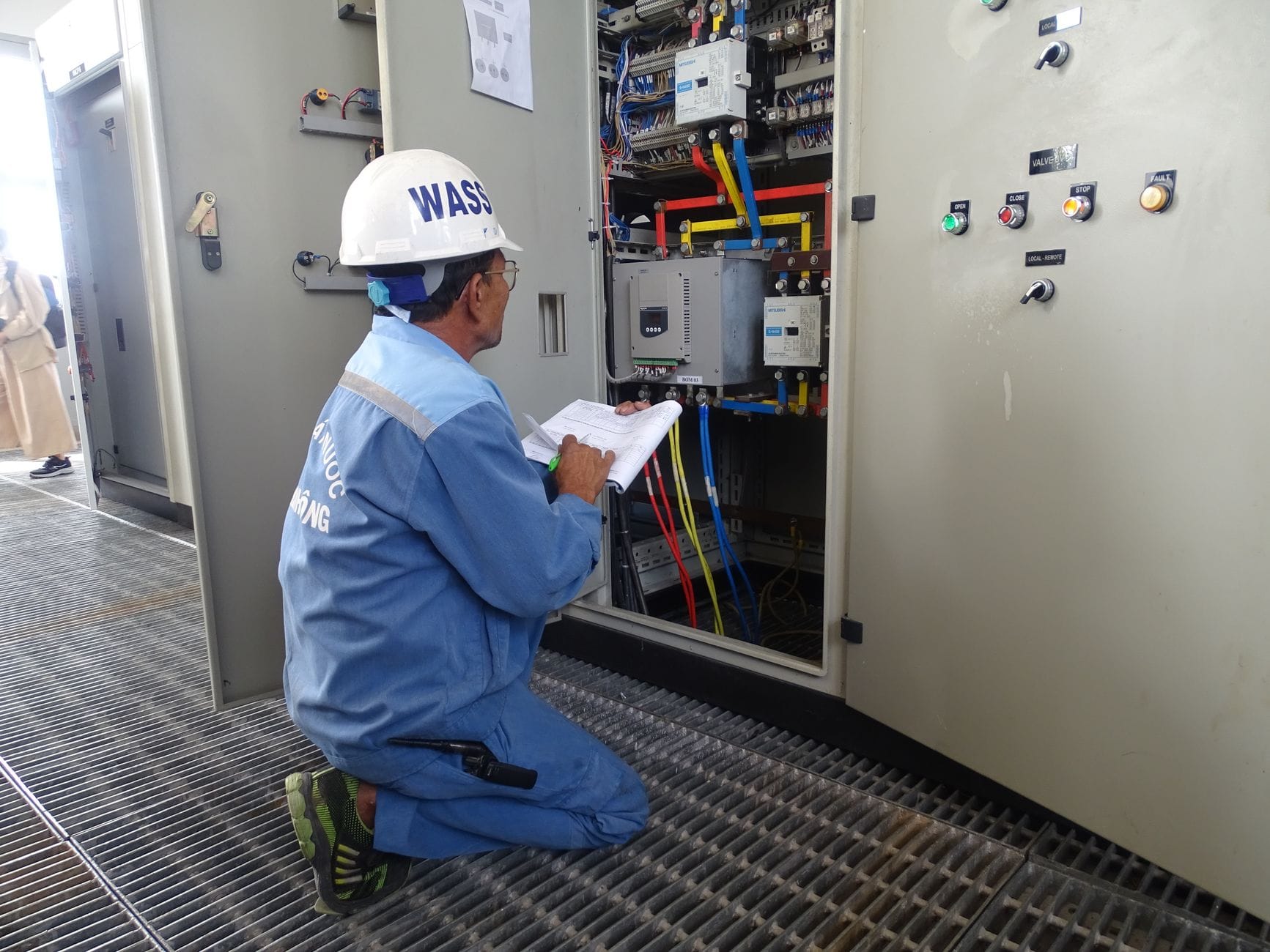 Engineer in uniform inspecting an electrical control panel in an industrial setting.