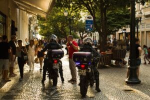 Municipal guards on motorcycles patrol a lively street in Brazil with bustling pedestrian activity.