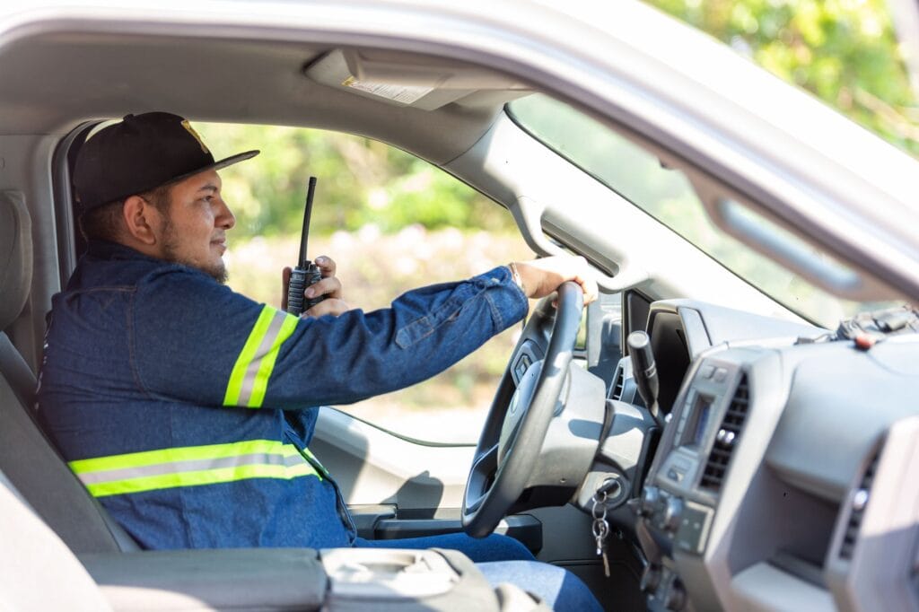A man in a uniform operates a vehicle while using a two-way radio for communication.