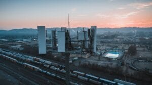 Drone view of contemporary cell tower located near railway tracks with cargo containers and wagons against sunset sky